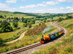 Miniature steam train with colorful carriages traveling through green countryside